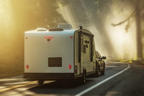 Car towing caravan with moody sunlight in trees - MitchMarket Finance